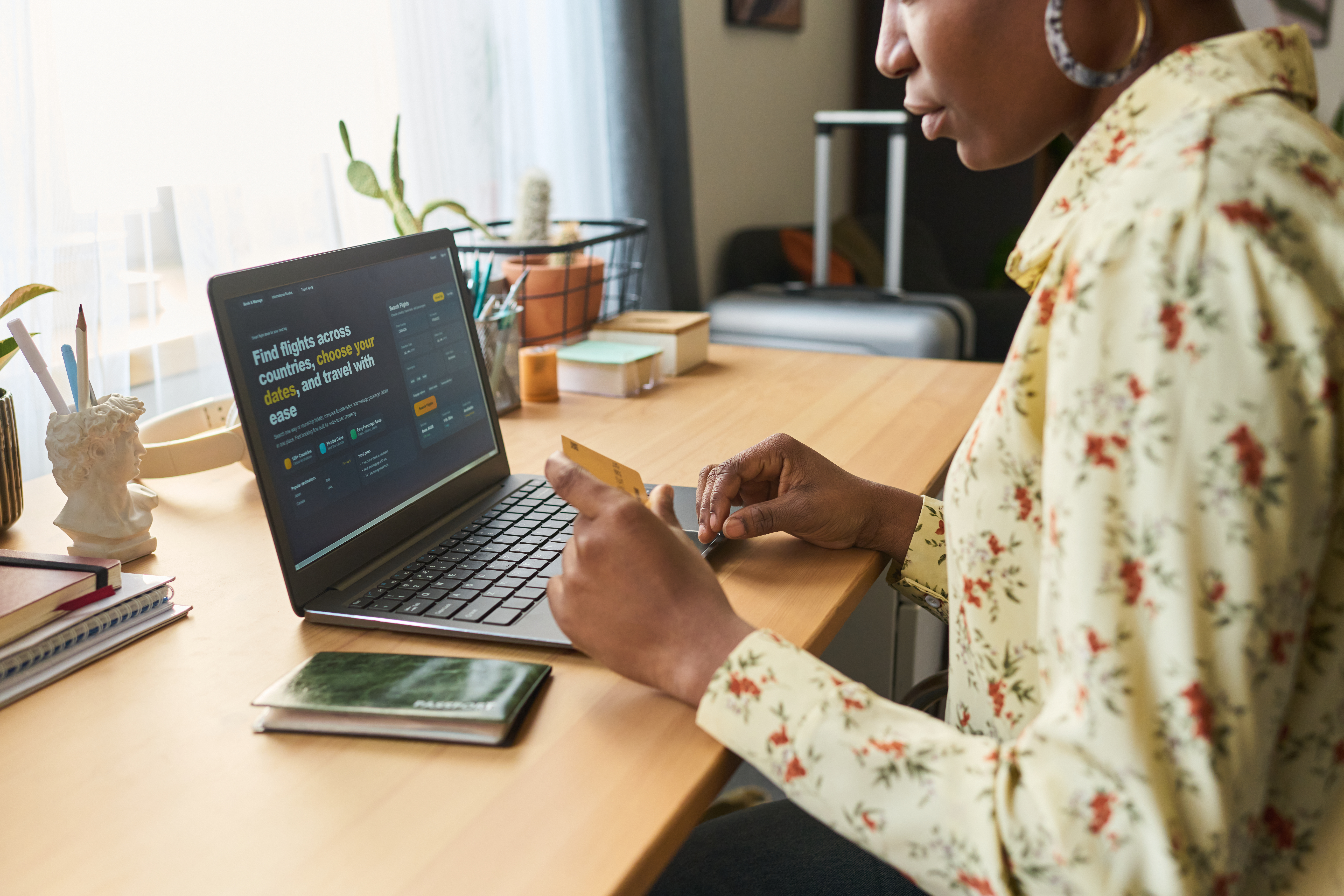 Young adult Black woman booking trip on laptop and holding credit card at desk, planning travel purchase. Ideal for tourism marketing, online booking, vacation budgeting